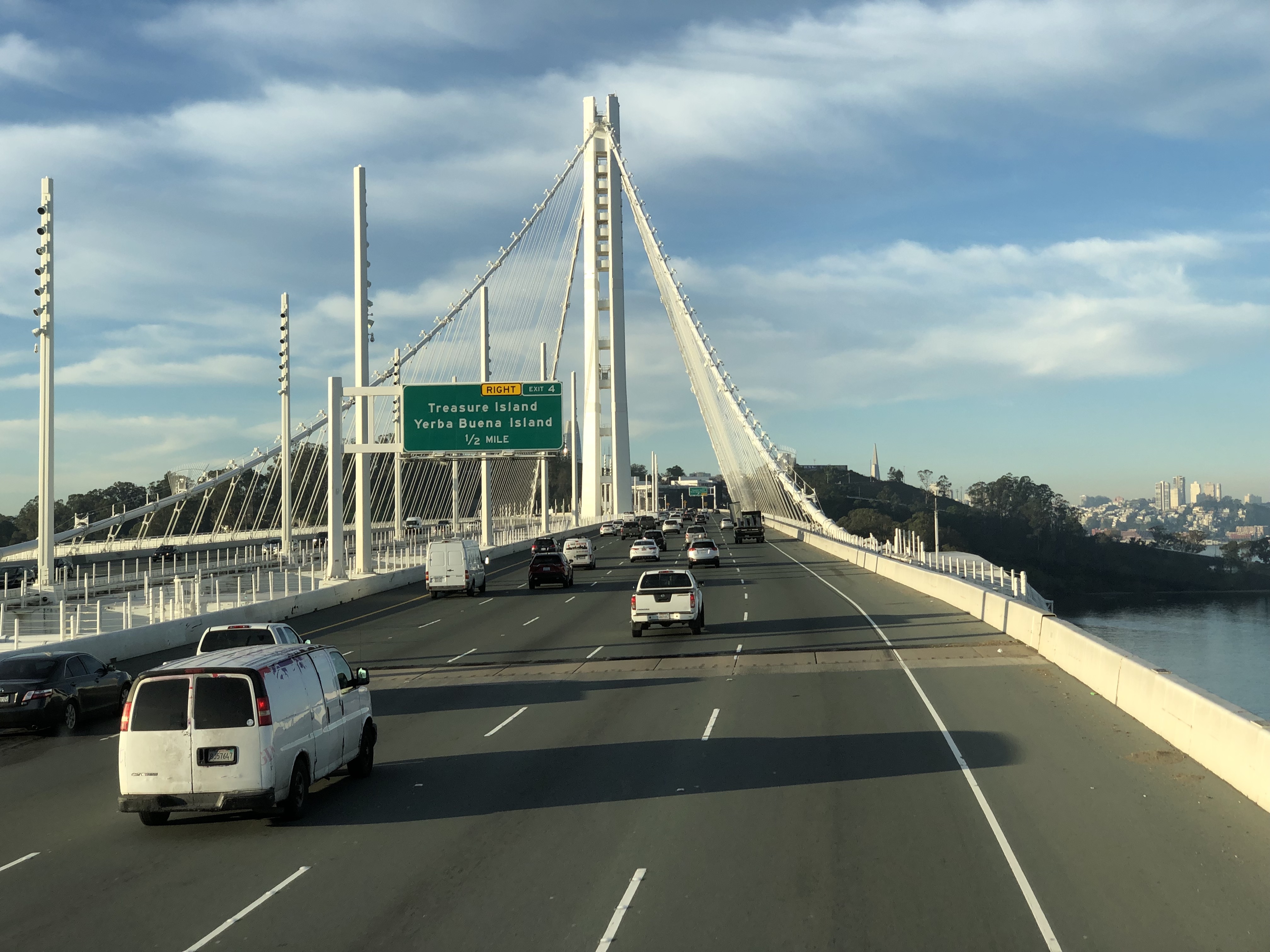 A person in a white sweater consults a mobile phone while writing on a notepad.